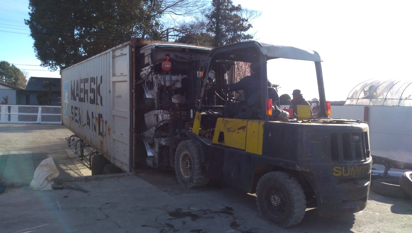 Forklift loading dismantled truck parts into a shipping container